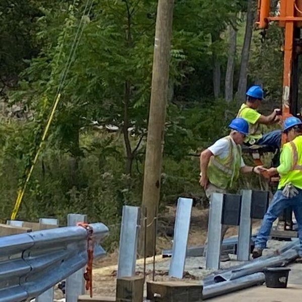 A team of workers installing guide rails near a wooded area.