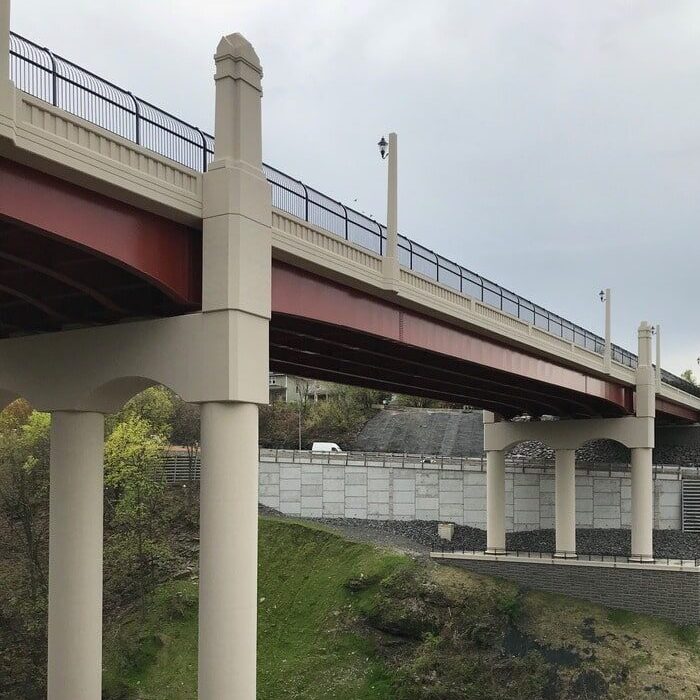 Modern bridge named the Harrison Avenue Bridge in Scranton, PA with red steel beams and concrete columns stretching over a lush, green valley.